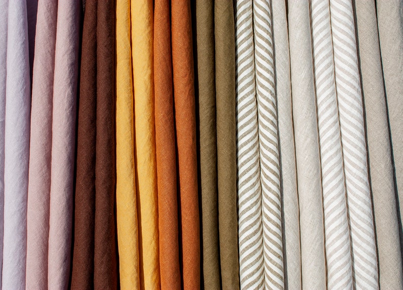 Pu&ograve; includere: Primo piano di vari campioni di tessuto in una gamma di colori, tra cui rosa chiaro, marrone, giallo e verde oliva. Alcuni campioni presentano un motivo a righe. I tessuti sembrano essere di lino o un materiale naturale simile.
