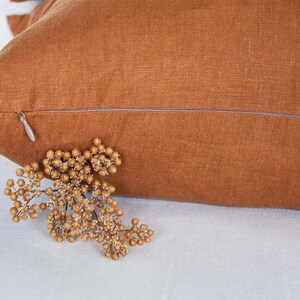 May include: A brown linen pillow cover with a zipper closure. The pillow cover is made from a soft, natural fabric and has a subtle texture.