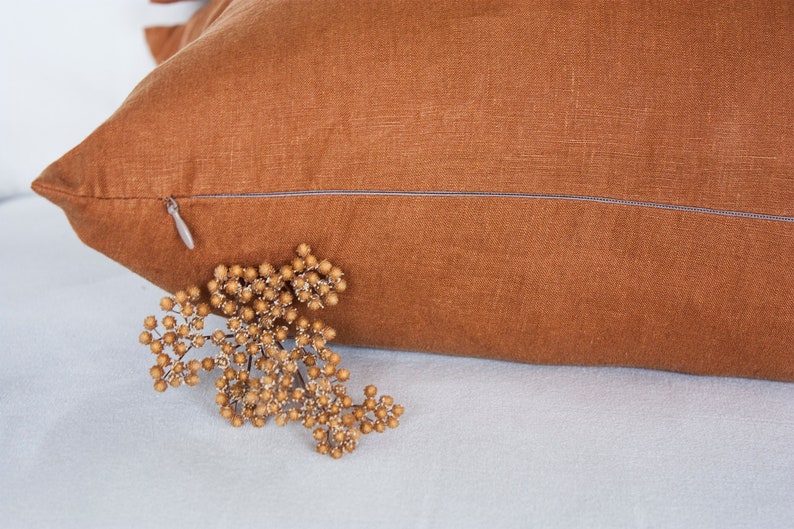 May include: A brown linen pillow cover with a zipper closure. The pillow cover is made from a soft, natural fabric and has a subtle texture.