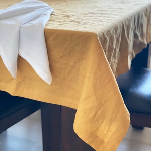 May include: A mustard yellow linen tablecloth draped over a wooden table with a white napkin folded on top.