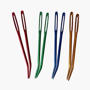 May include: A collection of six large-eye needles in various colors: red, green, blue, and gold. These curved needles are designed for easy threading and are ideal for yarn crafts and sewing projects.