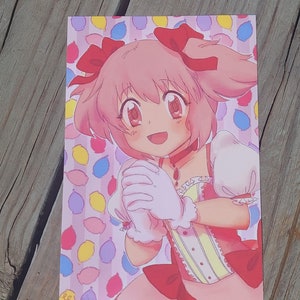 Op de afbeelding: Een anime-personage met roze haar, gekleed in een witte en roze jurk met rode strikken. Ze glimlacht en houdt haar handen bij elkaar. De achtergrond is een roze en wit patroon met kleurrijke ballonnen.