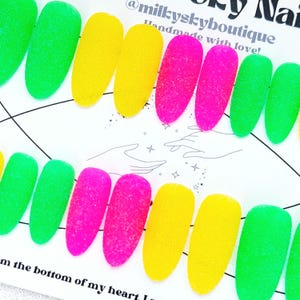 Puede incluir: Diez uñas postizas ovaladas en tres colores: verde, rosa y amarillo. Las uñas tienen un acabado texturizado y azucarado. El texto "@milkskyboutique Hecho a mano con amor!" es visible en la imagen.