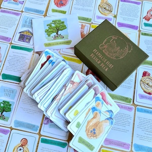 May include: A green box with the text "Permaculture Design Deck" on the front. The box contains a deck of cards with watercolor illustrations and text. The cards are spread out on a wooden table with other cards that have different designs and text.