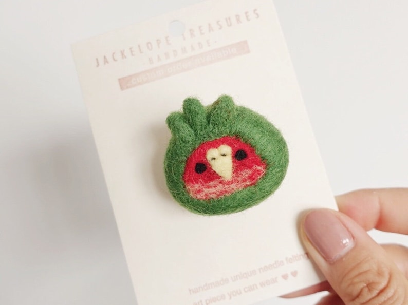 May include: A green felt pin with a red and yellow bird design. The pin is handmade and says "Jackelope Treasures Handmade" on the card.