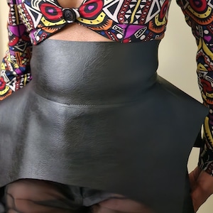 May include: A black leather skirt with a geometric patterned top. The top has a V-neck and a button closure. The skirt has a high waist and a flared hem.