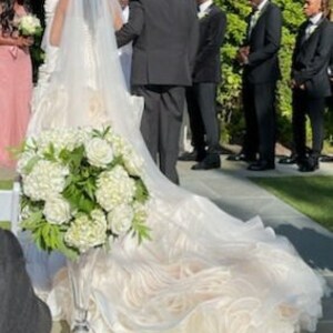 May include: A white wedding dress with a long train and a bouquet of white flowers. The dress has a fitted bodice and a full skirt.