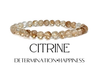 May include: A Citrine gemstone bracelet. The bracelet features round, translucent beads in shades of light brown and amber. The word "CITRINE" is displayed below the bracelet, along with the words "DETERMINATION•HAPPINESS."
