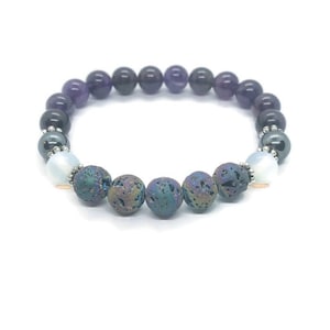 May include: A beaded bracelet featuring a mix of natural stone beads. The bracelet includes dark purple amethyst, iridescent lava rock, and white opal beads. The beads are strung together with a silver-colored metal spacer.