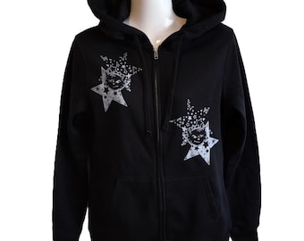 May include: Black zip-up hoodie with a hood and front pockets. The hoodie features a white graphic of a cat face inside a starburst design on the chest. The zipper is silver.