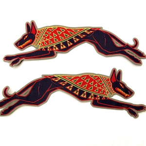 May include: Two black stylized illustrations of a dog running, wearing a red, yellow, and green patterned collar. The dog is running to the right.
