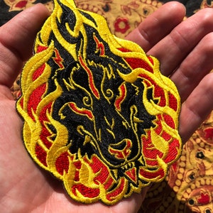 May include: Embroidered patch featuring a black wolf's head engulfed in flames. The flames are detailed with yellow and red thread, creating a striking contrast against the black. This patch is suitable for jackets, bags, or other fabric items.