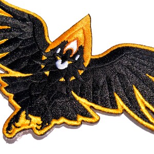 May include: Black and gold embroidered patch of a stylized eagle with its wings spread wide.