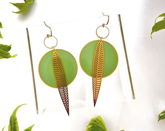 May include: A pair of gold earrings with a green leaf design. The earrings are circular with a leaf cut out in the center. The leaves are attached to a long, thin, gold bar.