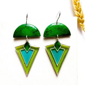 May include: A pair of contemporary earrings with a geometric design. Each earring has a green, semi-circular top, connected to a lime green and turquoise triangle with silver edging. The earrings hang from silver hooks.