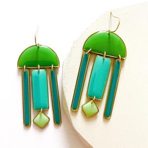 May include: A pair of geometric earrings with a brass frame. The earrings feature a green half-circle at the top, with teal rectangles and green diamond shapes hanging below. The earrings are approximately 7.6 cm long.