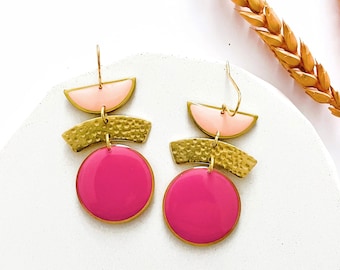 May include: Gold earrings with pink and gold geometric shapes. The earrings feature two round pink discs and three gold shapes, including two half-circles and one curved rectangle.