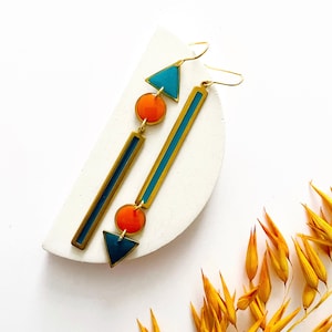 Puede incluir: Un par de pendientes de oro con formas geométricas y esmalte naranja y turquesa. Los pendientes tienen una barra larga, un círculo, un triángulo y un círculo más pequeño.