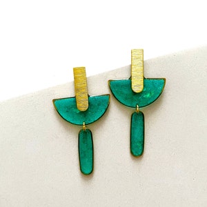 May include: A pair of green and gold geometric earrings. The earrings feature a half-circle shape with a gold bar and a dangling green rectangle.