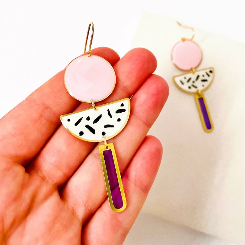 Puede incluir: Un par de pendientes de oro con esmalte rosa, blanco y morado. Los pendientes tienen forma de c&iacute;rculo, semic&iacute;rculo y rect&aacute;ngulo.