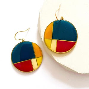 May include: A pair of gold tone earrings with a round, geometric design. The earrings are made of teal, red, yellow, and cream enamel.