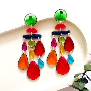 Puede incluir: Un par de pendientes colgantes coloridos con cuentas de vidrio en forma de lágrima y redondas en tonos de verde, azul, rojo, naranja, amarillo y rosa. Los pendientes están suspendidos de aros de metal plateados.