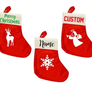 May include: Three red Christmas stockings with white cuffs and red hanging loops. One stocking has "Merry Christmas" in green and a white reindeer. Another says "Custom" in red with a white angel. The third says "Name" with a white snowflake.