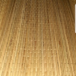 May include: A close-up of a woven bamboo mat with a natural, light brown color. The mat is made of thin strips of bamboo that are woven together in a tight pattern.