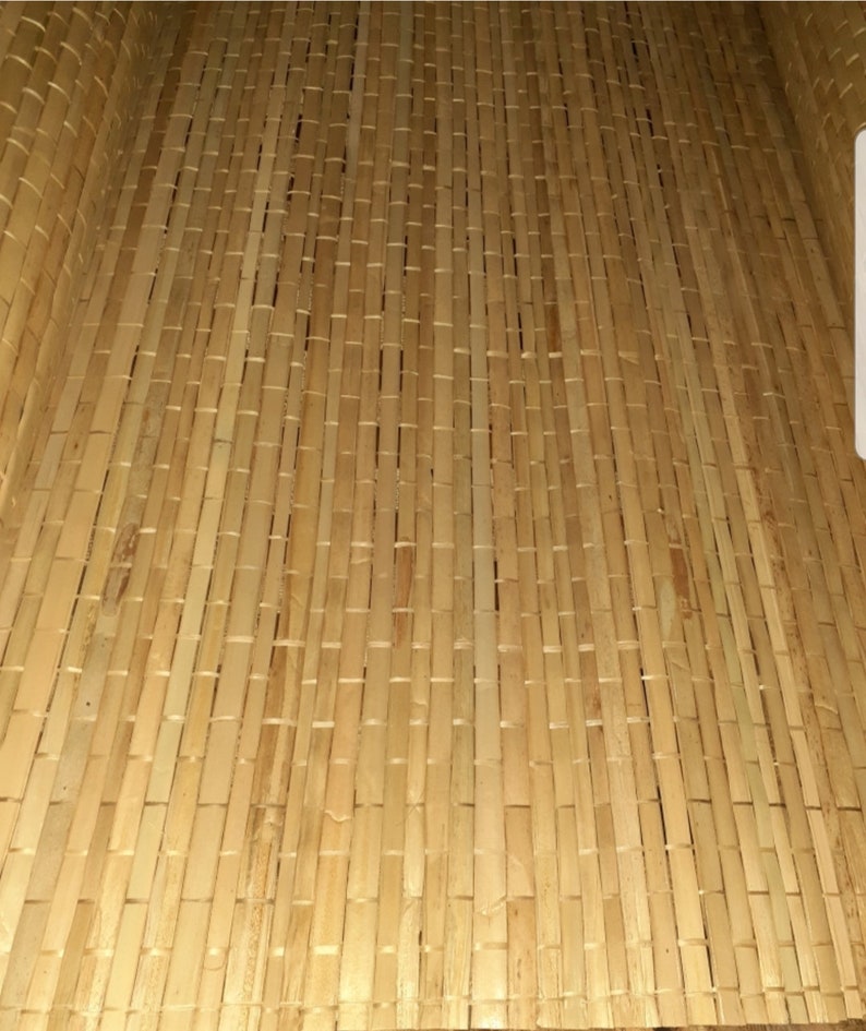 May include: A close-up of a woven bamboo mat with a natural, light brown color. The mat is made of thin strips of bamboo that are woven together in a tight pattern.