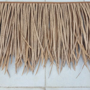May include: A close-up of a brown thatched roof panel made of natural palm leaves. The panel is made of long, thin strips of palm leaves that are woven together to create a dense, textured surface.
