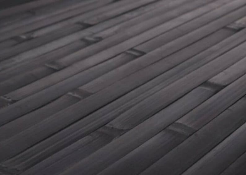 May include: Close-up of a dark gray bamboo mat. The bamboo strips are arranged diagonally, creating a textured surface. The mat's color is a deep, neutral gray, suitable for various interior design styles.