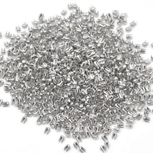 May include: A large pile of silver metal rivets, also known as nailheads, used for decorative and functional purposes in crafts and leatherwork.
