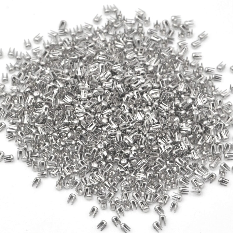 May include: A large pile of silver metal rivets, also known as nailheads, used for decorative and functional purposes in crafts and leatherwork.