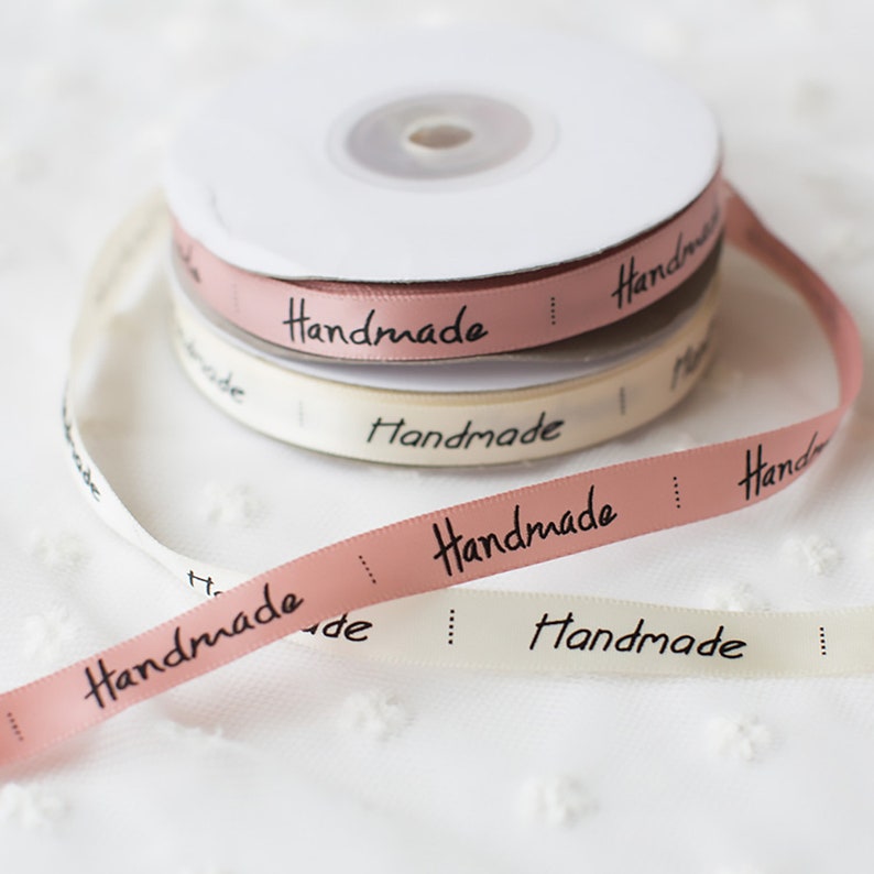 May include: Four spools of ribbon with the word "Handmade" printed on them. The ribbon is in two colors: pink and white.