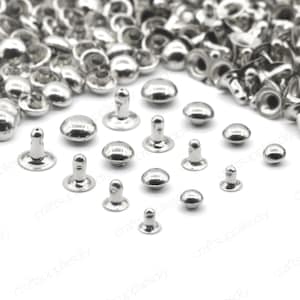 Peut inclure: Un assortiment de rivets en métal argenté de différentes tailles et formes. Les rivets sont disposés en demi-cercle sur un fond blanc.