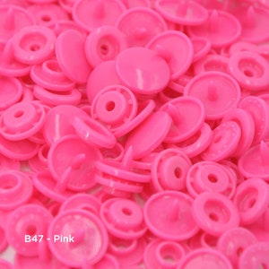 May include: A close-up image of a large pile of pink plastic snap buttons. The buttons are all the same size and shape, and they have a smooth, shiny finish. The text "B47 - Pink" is visible in the lower left corner of the image.
