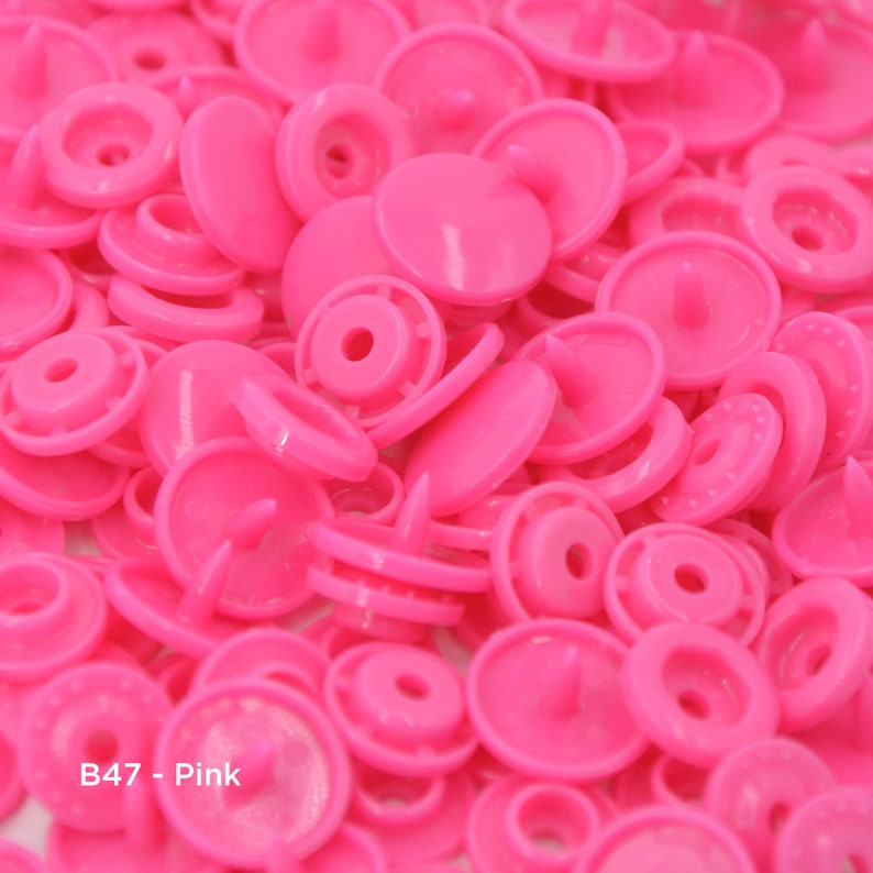 May include: A close-up image of a large pile of pink plastic snap buttons. The buttons are all the same size and shape, and they have a smooth, shiny finish. The text "B47 - Pink" is visible in the lower left corner of the image.