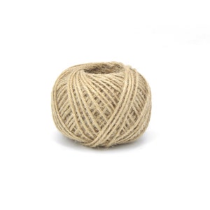 May include: A ball of natural twine made from jute fibers. The twine is a light brown color and is tightly wound into a ball shape.
