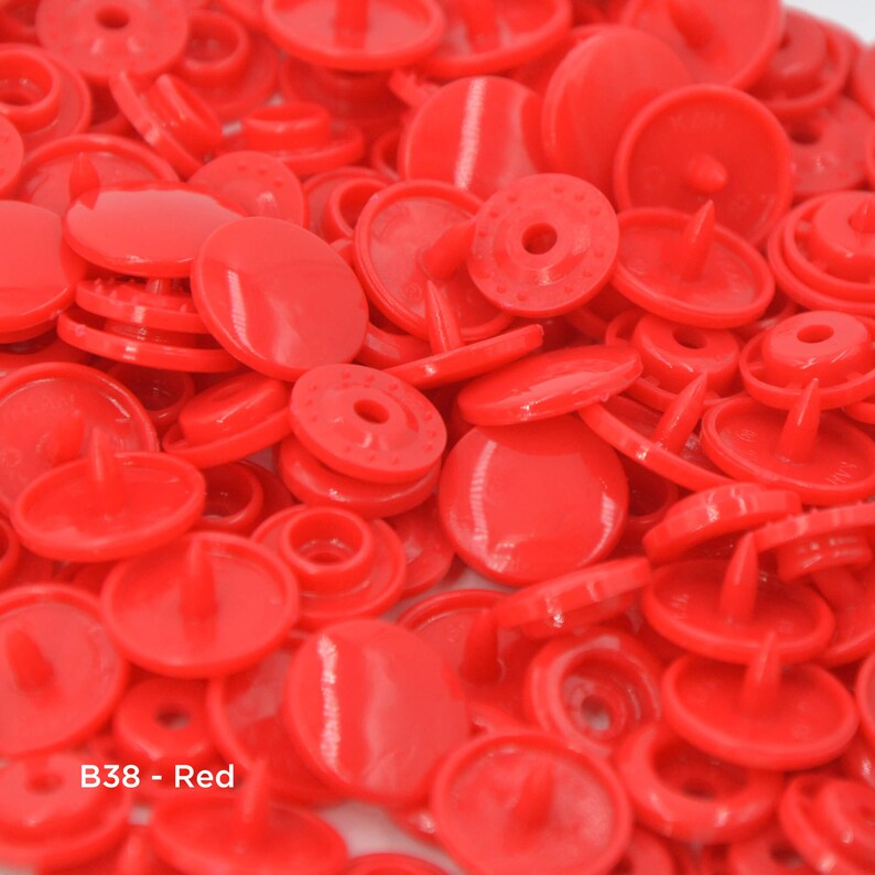 May include: A large pile of bright red plastic snap buttons. The buttons are all the same size and shape, and they have a smooth, glossy finish. B38 - Red.