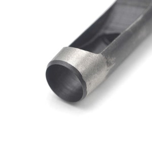 May include: Close-up of a silver and black metal hole punch tool. The tool is designed to punch holes in leather or other materials.