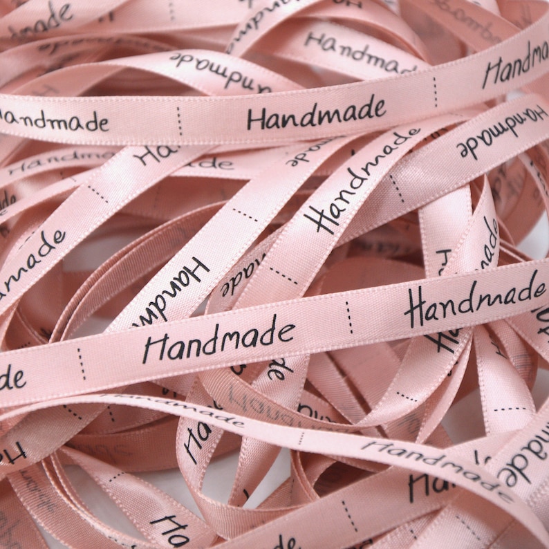 May include: A pile of pink satin ribbon with the word "Handmade" printed in black on each ribbon.