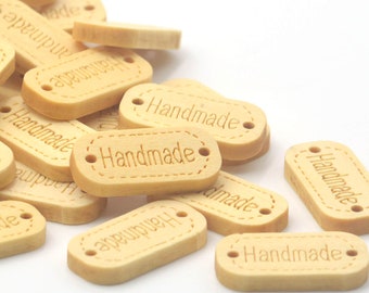 May include: A collection of small, light-colored wooden tags with the word "Handmade" engraved on them. Each tag has a stitched border design and two small holes for attaching. The tags are scattered on a white background.