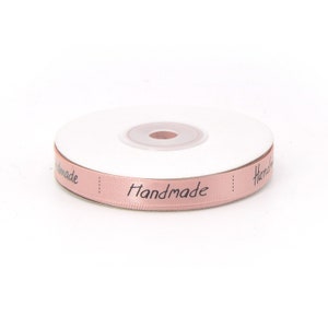 May include: A spool of pink satin ribbon with the word "Handmade" printed in black lettering.