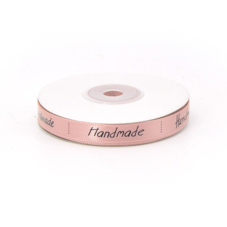 May include: A spool of pink satin ribbon with the word "Handmade" printed in black lettering.