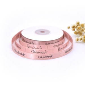 May include: A roll of pink satin ribbon with the word "Handmade" printed in black on it.