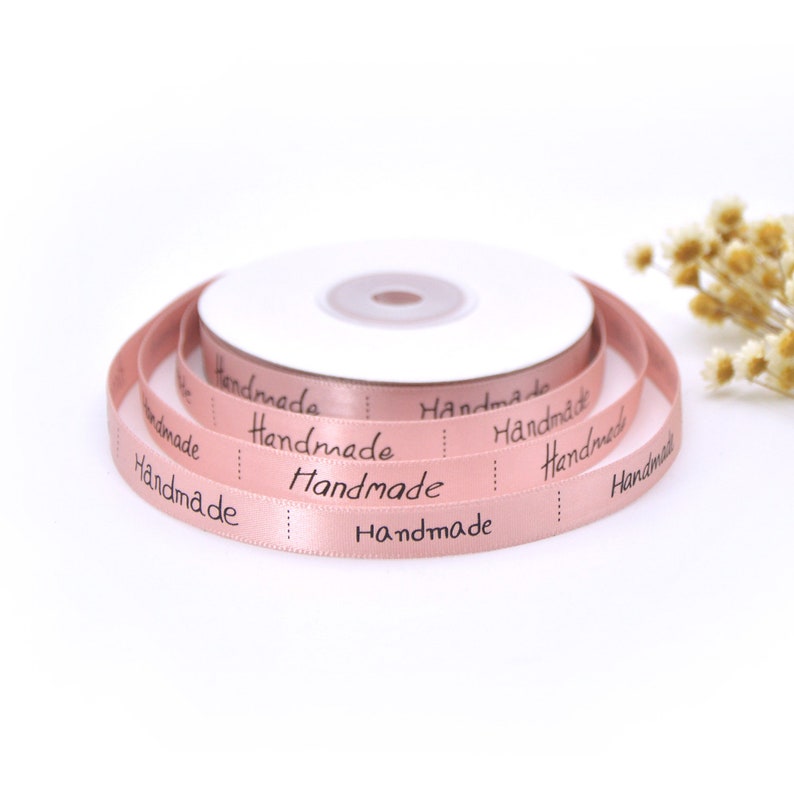 May include: A roll of pink satin ribbon with the word "Handmade" printed in black on it.