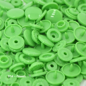 May include: A close-up view of a large quantity of green plastic snap buttons. The buttons are all the same size and shape, and they have a small, raised center.