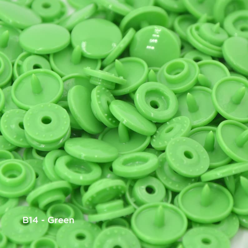 May include: A close-up view of a large quantity of green plastic snap buttons. The buttons are all the same size and shape, and they have a small, raised center.
