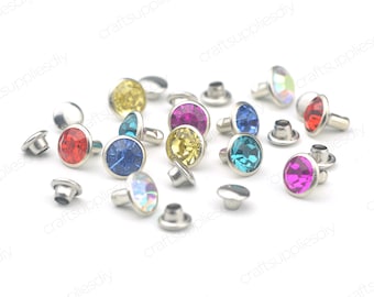 May include: Assortment of colorful rhinestone rivets with silver settings. The rhinestones are in various colors, including red, pink, blue, green, yellow, and clear.