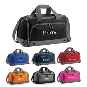 Op de afbeelding: Een verzameling gepersonaliseerde sporttassen in verschillende kleuren, waaronder zwart, blauw, rood, oranje, grijs en roze. Elke tas heeft een naam op de voorkant, met de naam "Harry" prominent weergegeven op de zwarte tas.